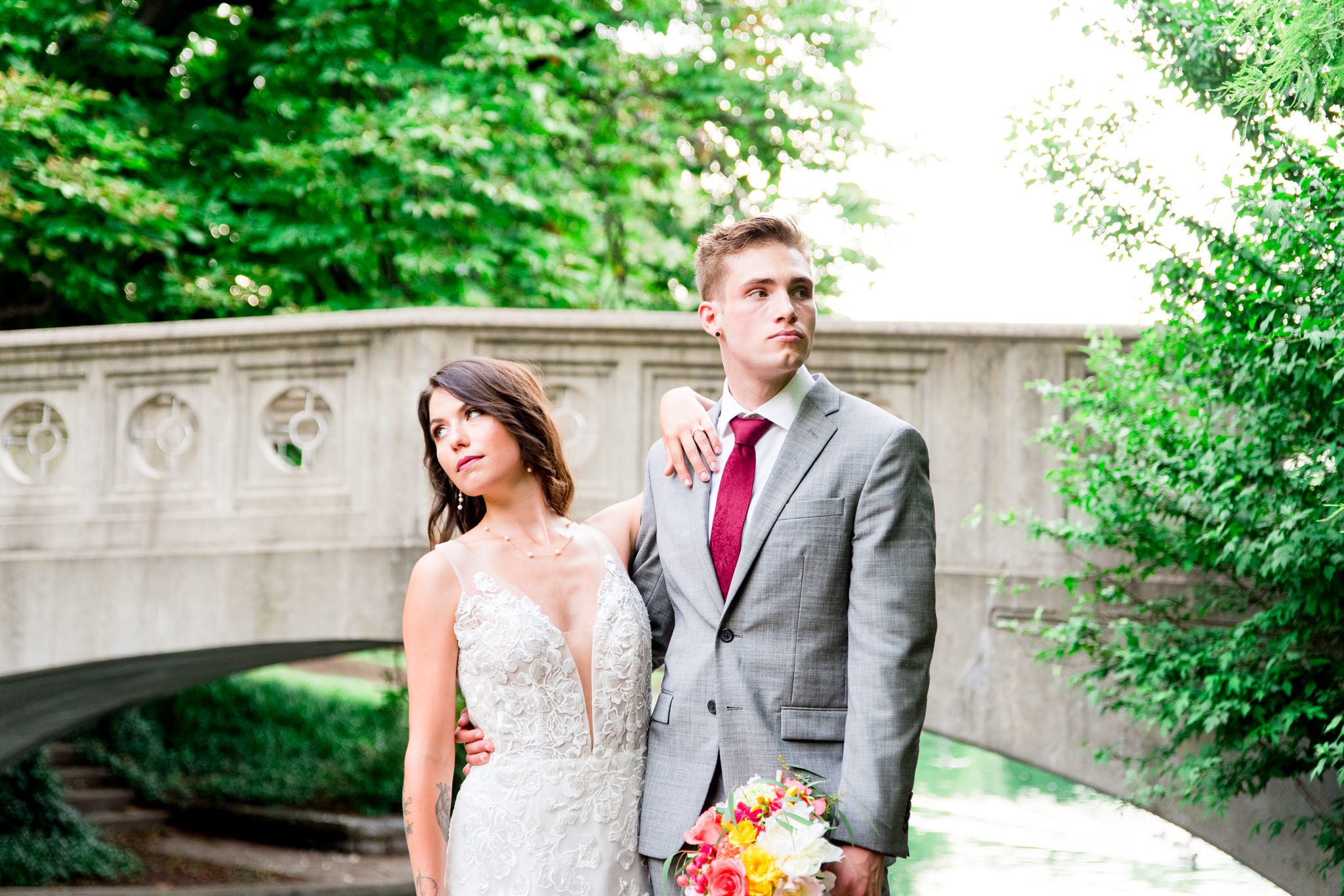 bride and groom stand together looking in opposite directions in front of bridge at Eden park
