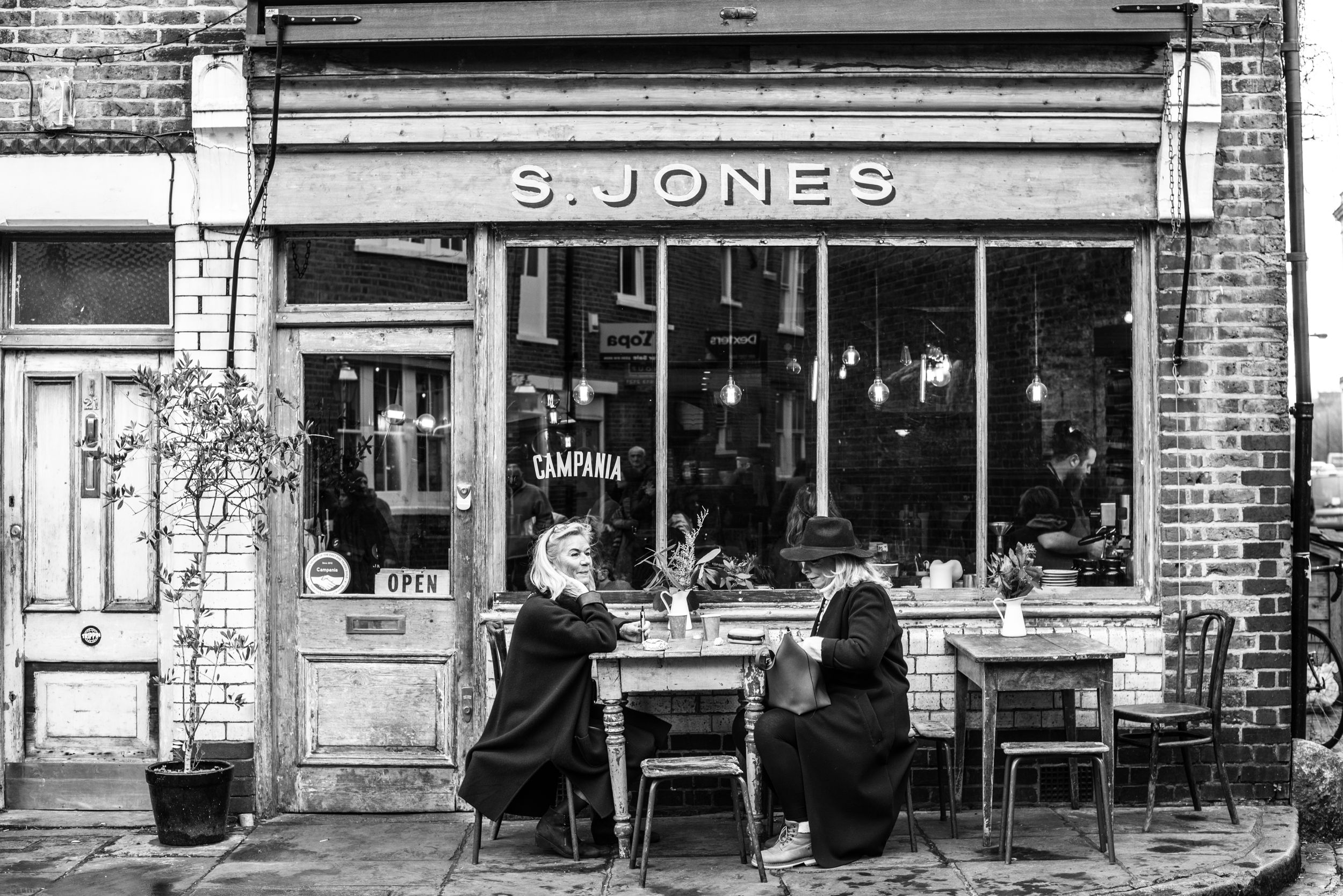 black and white image of two women lunching at an outside table at S. Jones in London's Flower Market area