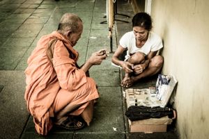 Monk looks at street sellers items on the streets of Bangkok Thailand