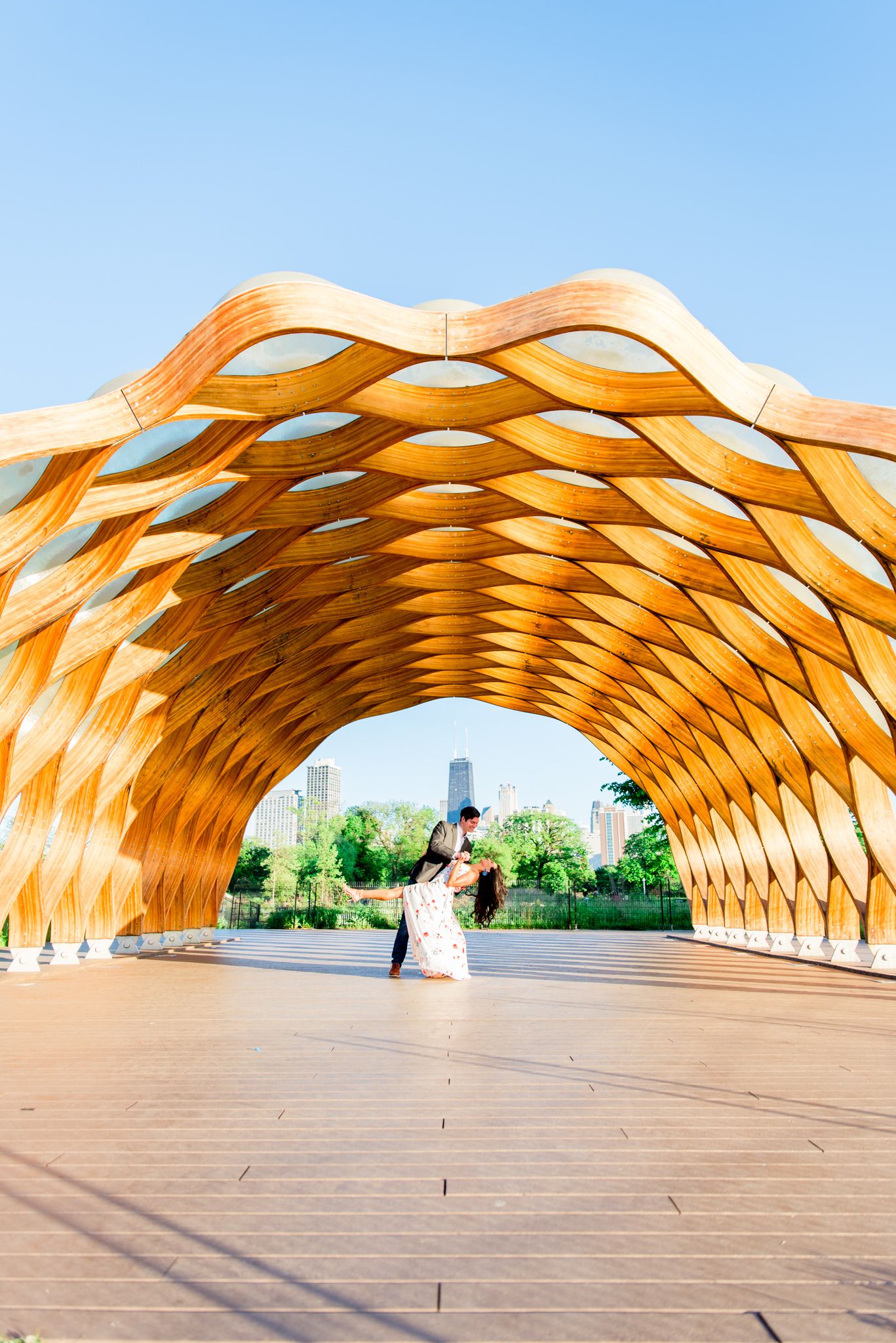 man in suit dipping and kissing woman under Honeycomb at Lincoln Park for engagement pictures in Chicago at sunset