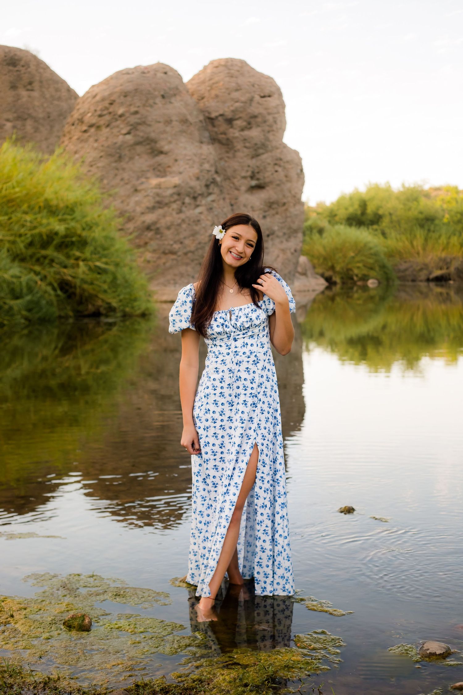 Senior graduate girl in a beautiful flowing dress standing and posing in the river at sunset in Arizona.