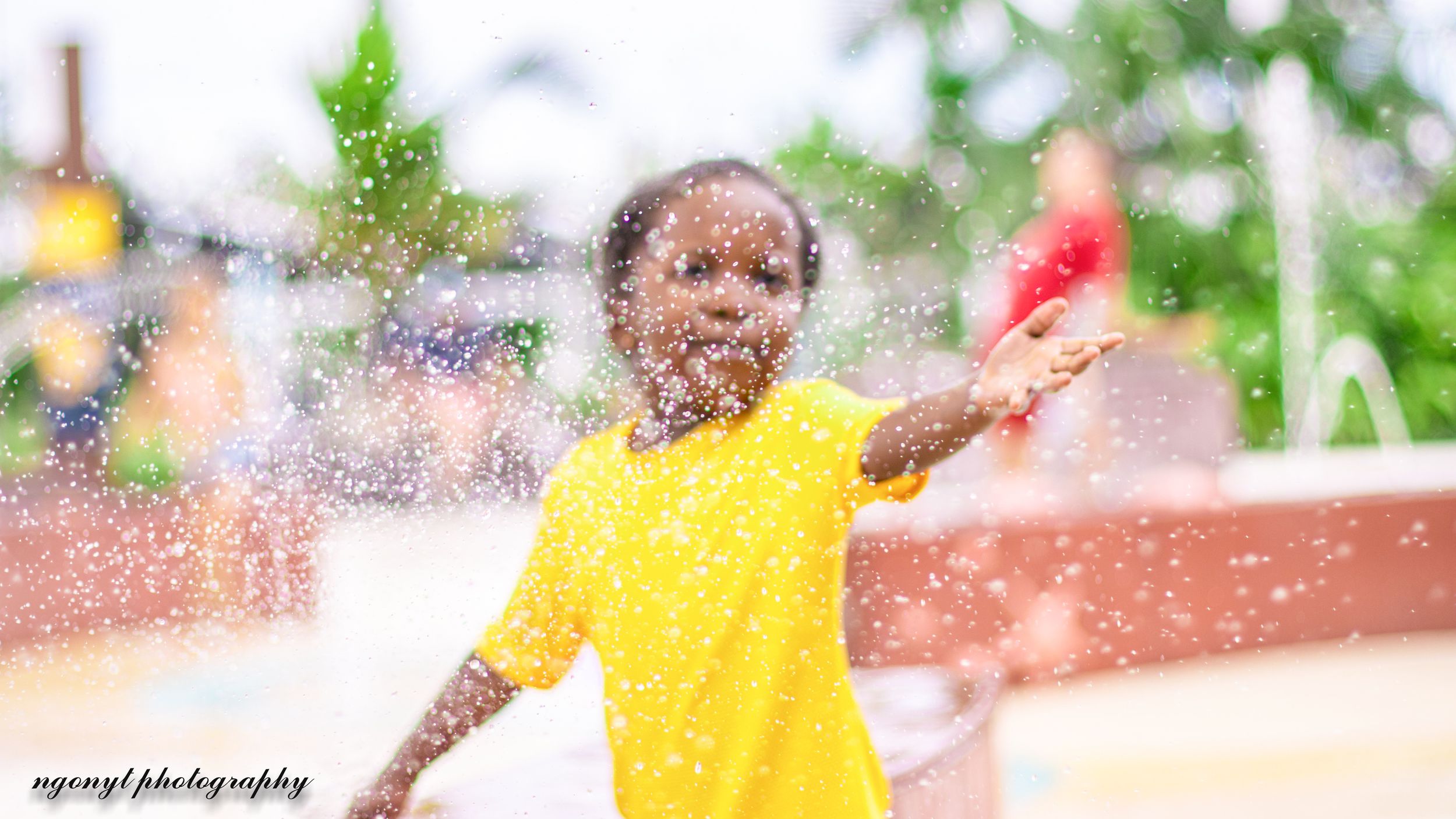 Child in yellow shirt playing in water with splashes all around.