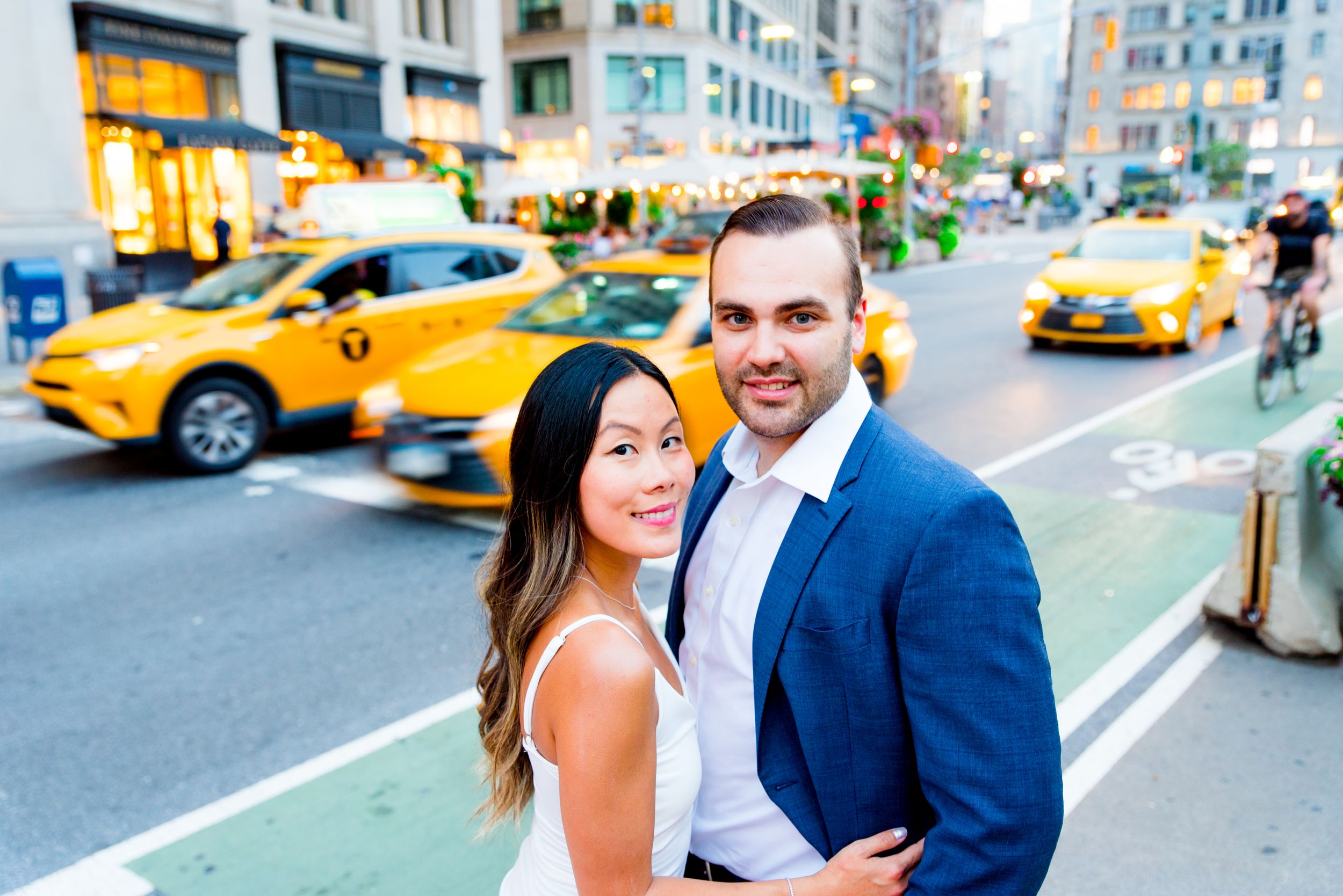 young engaged man and woman smiling at camera in front of yellow taxis in downtown Manhattan at sunset