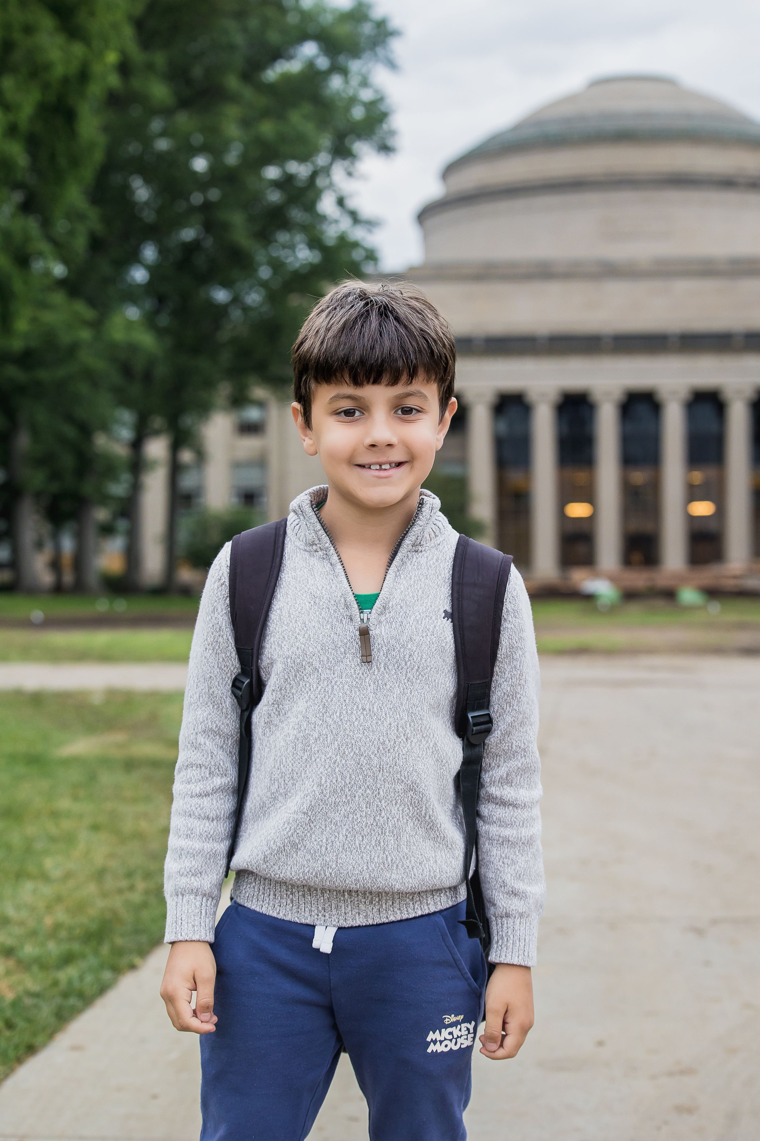 Young student with backpack stands in front of MIT's Great Dome building.