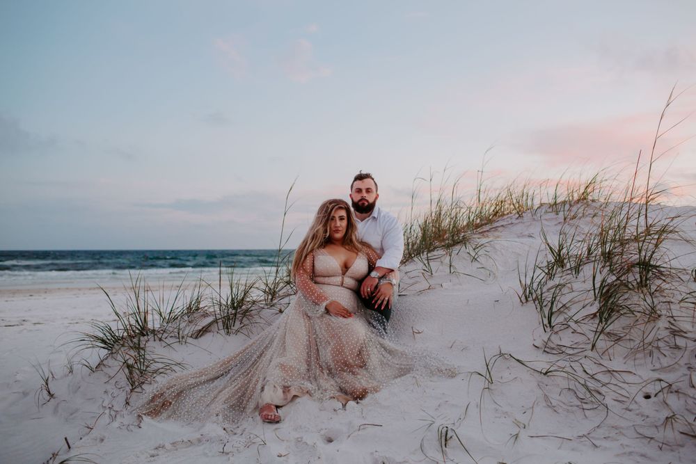 couple sitting in sand dunes at sunset
