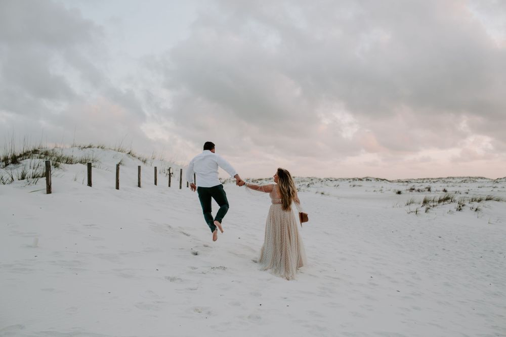 couple running in the dunes while the man jumps