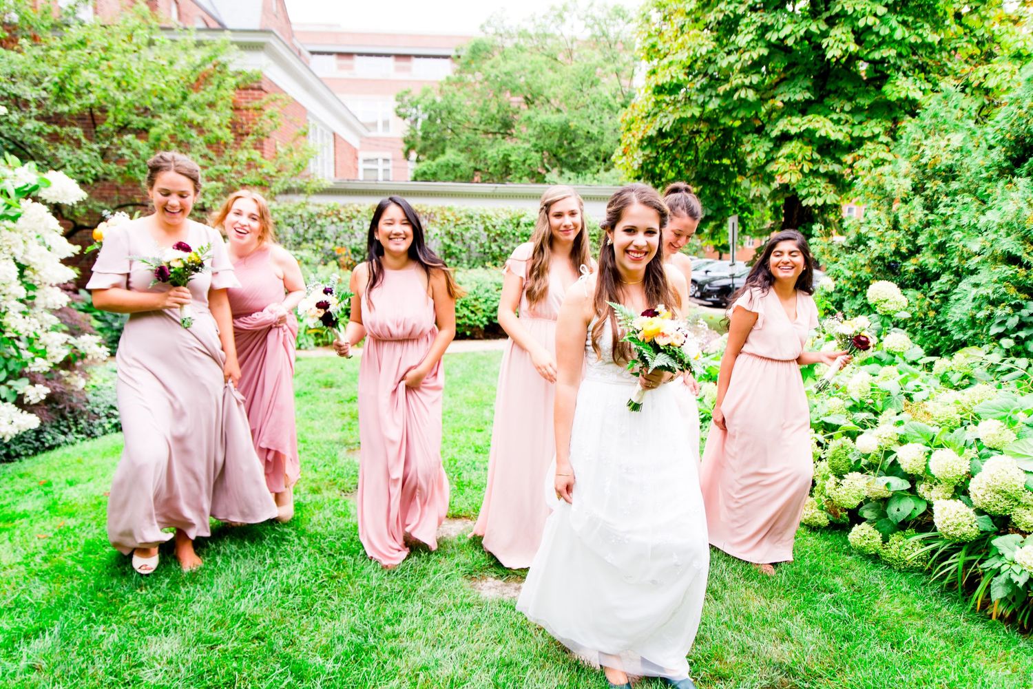 bride and bridesmaids in blush dresses walk through the garden during a brunch wedding at Woman's Club of Evanston