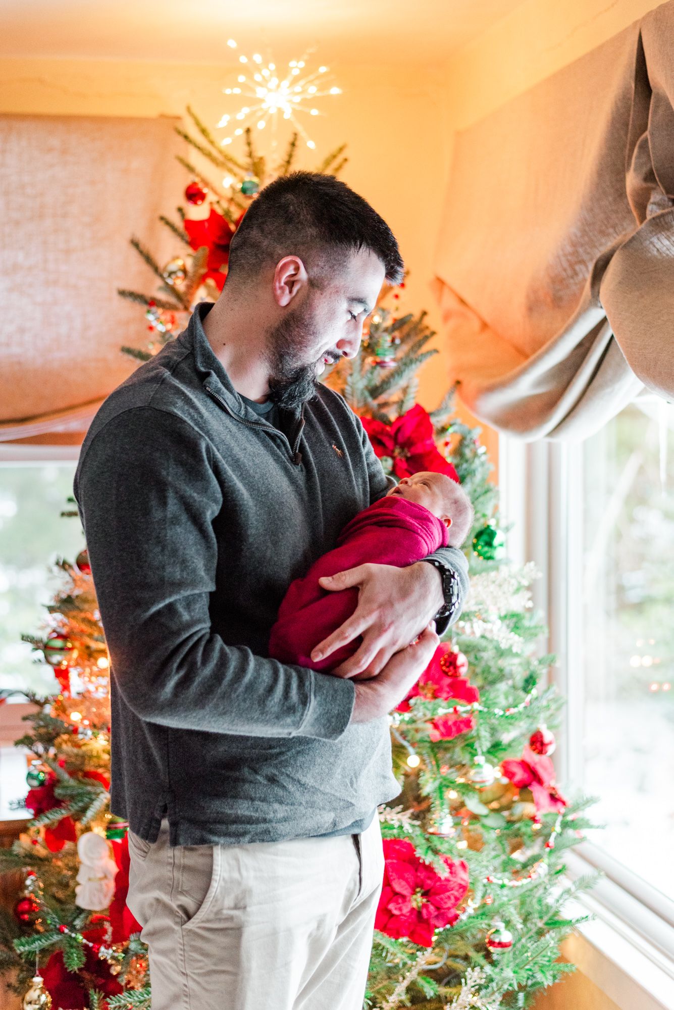 Lifestyle father holding newborn baby in pink wrap in front of Christmas tree in Pittsburgh, Pennsylvania