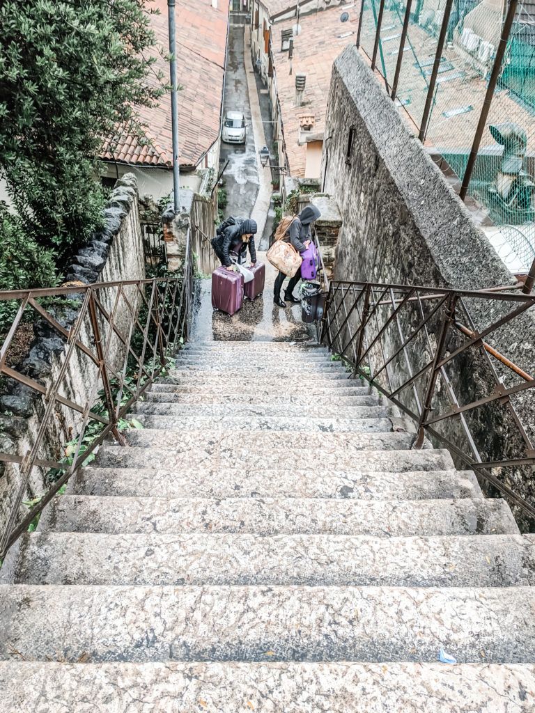 Three girls pulling luggage up a steep set of wet stairs in Verona, Italy