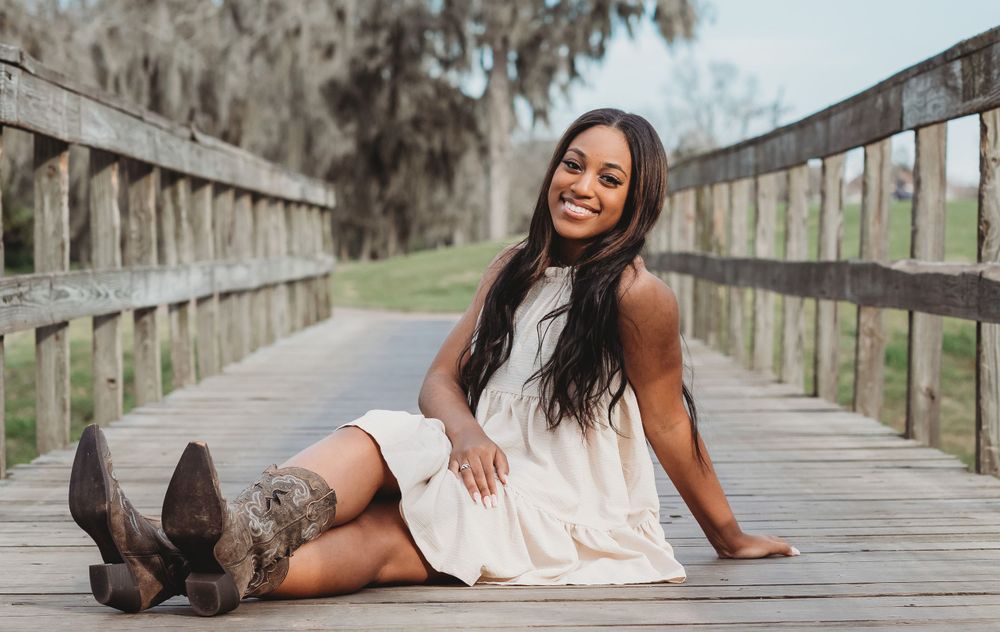 RidgePoint High School Senior Girl in a Burgundy Hat, Beige Dress, and Cowboy boots on bridge in Sienna Plantationer