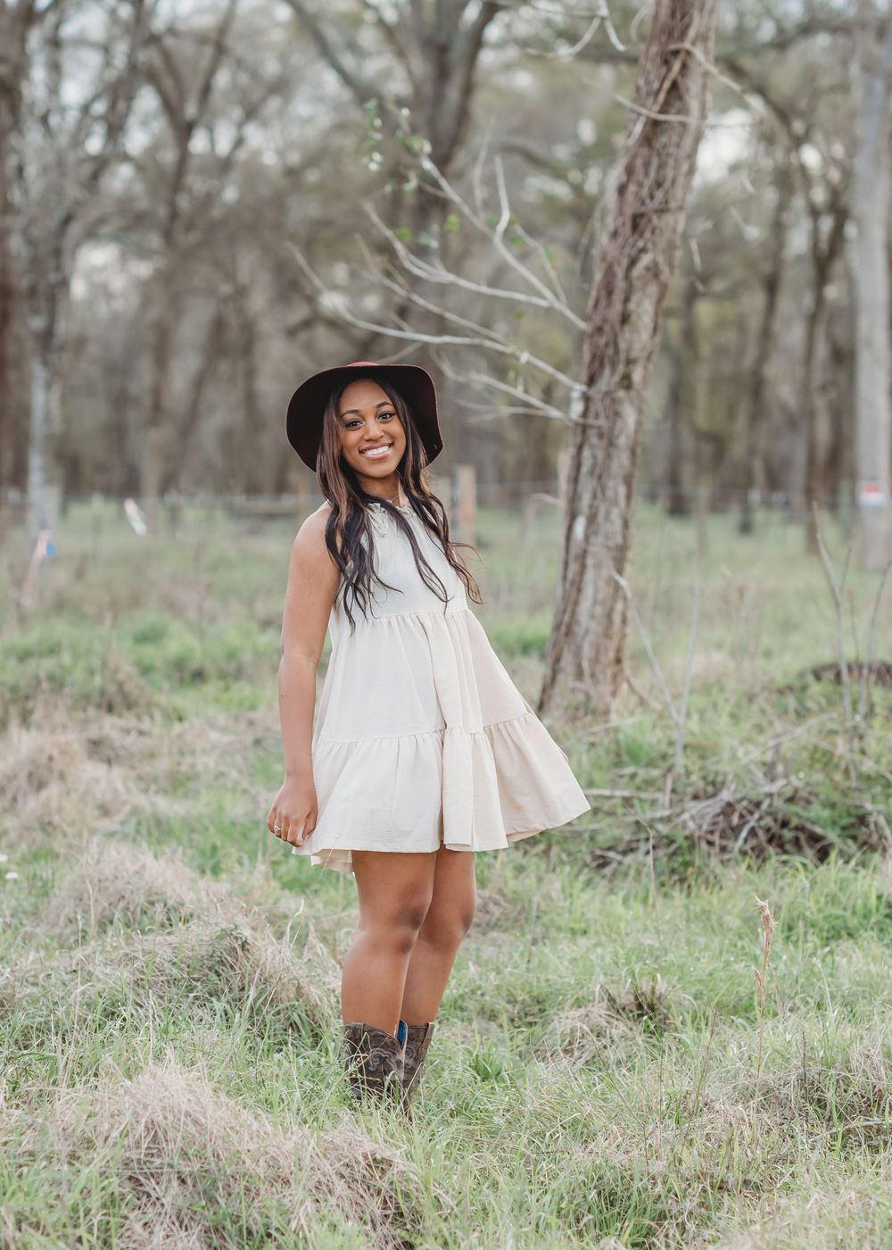 RidgePoint High School Senior Girl in a Burgundy Hat, Beige Dress, and Cowboy boots in woods in Sienna Plantation