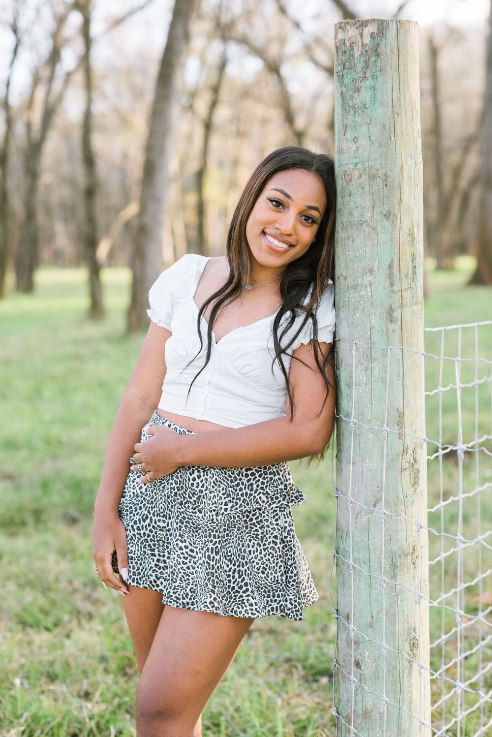 RidgePoint High School Senior Girl in white top and blue skirt pose on a fence in the woods in Sienna Plantation