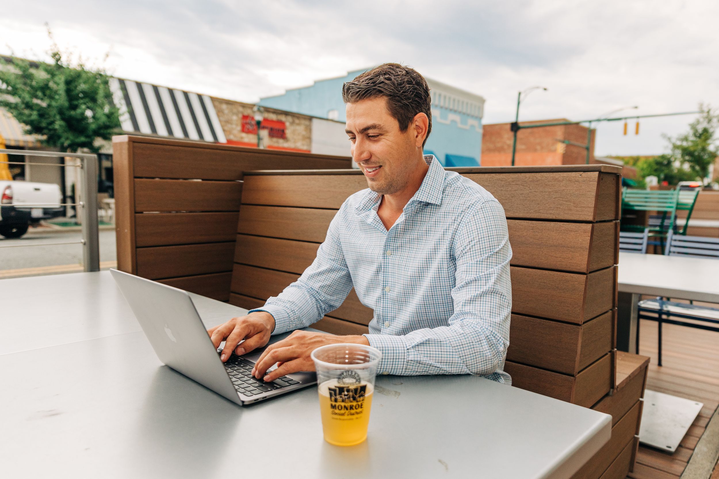 Man smiling and laughing while sitting with his computer and a beer in downtown Monroe, NC