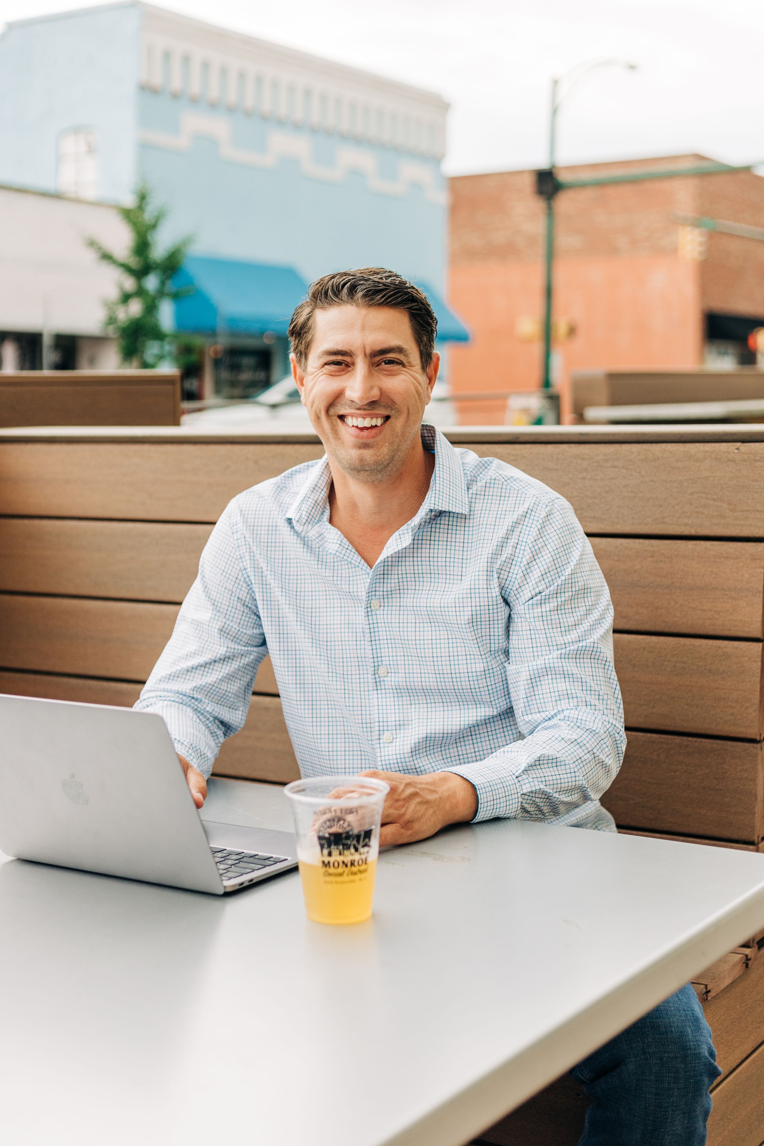 Man smiling and laughing while sitting with his computer and a beer in downtown Monroe, NC