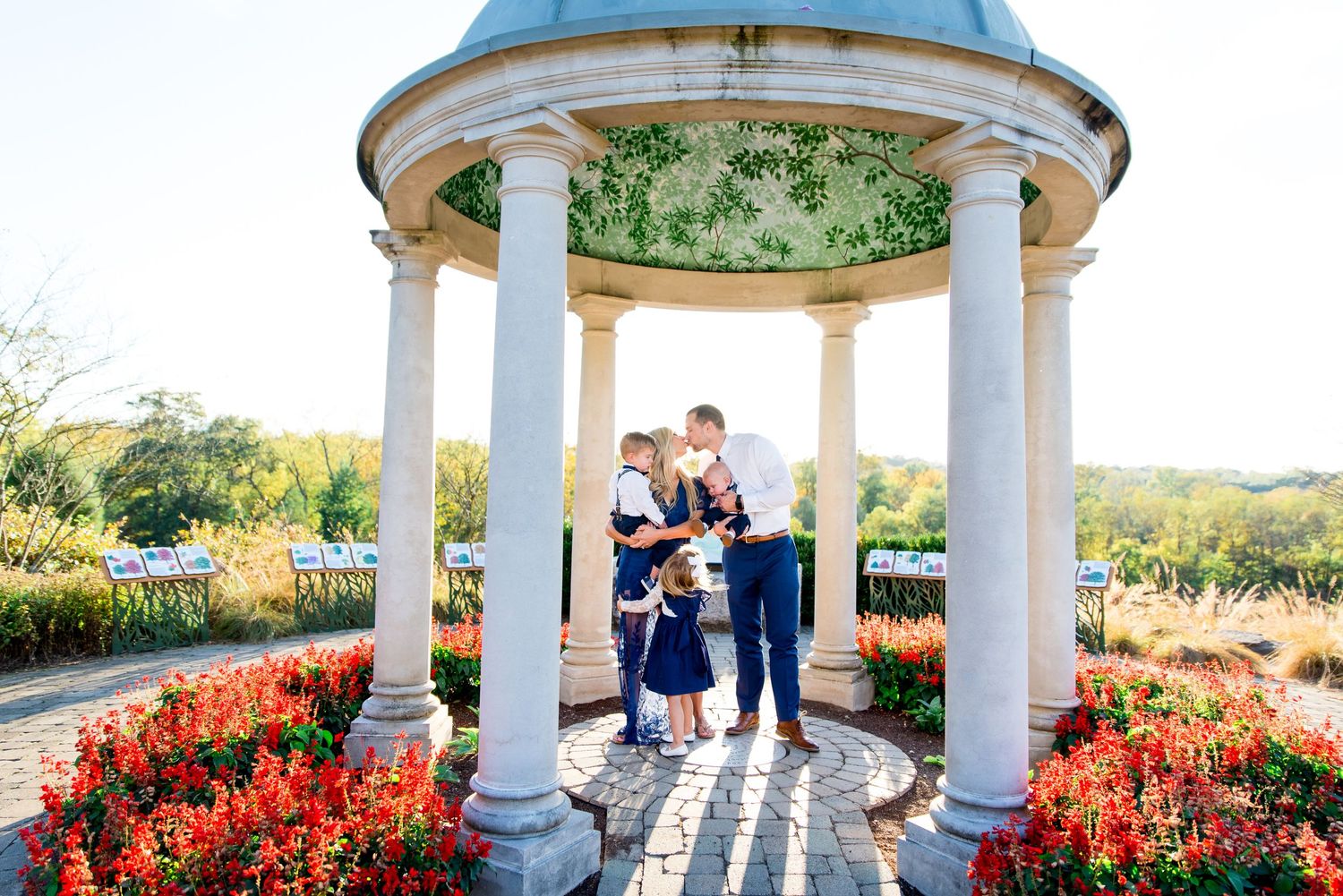 mother and father kissing and holding their three kids under a gazebo at sunset