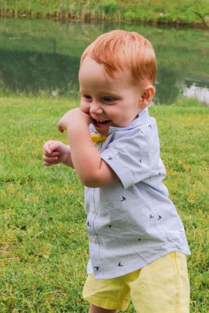 A joyful toddler in gray shirt and yellow shorts plays outdoors near a pond.