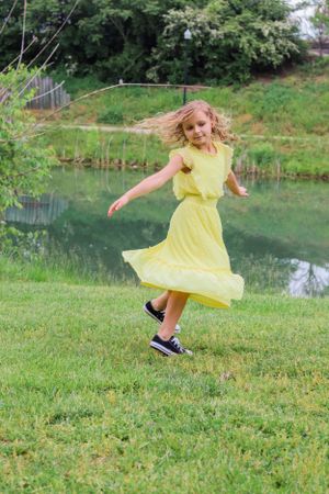 A twirling dancer in a flowing yellow dress performs on grass near a pond.