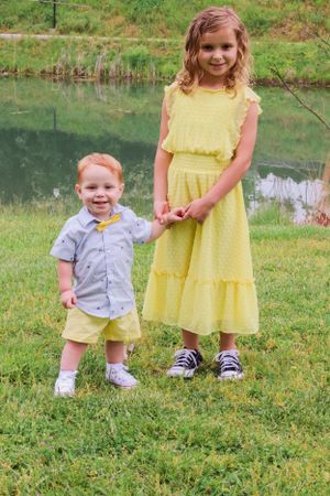 Two children in coordinating yellow and gray outfits standing together by a pond.