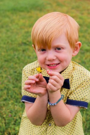A child in yellow polka dot shirt holding something small while smiling outdoors.