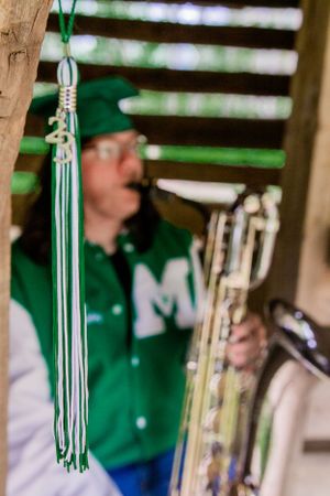 Green and white graduation tassel hanging with saxophone in soft focus.