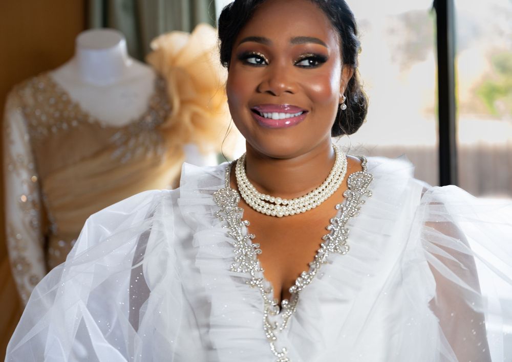 A radiant smile shines through as someone wears an elegant white wedding gown with pearl necklace and upswept hairstyle.