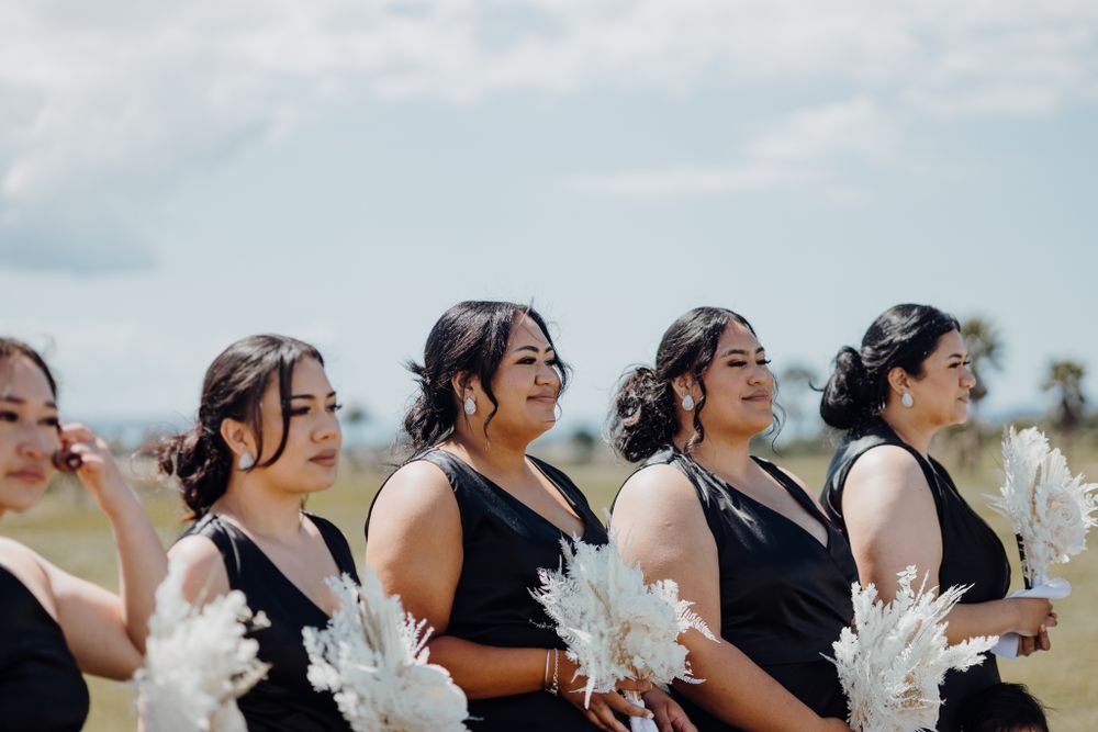 Bridesmaids in black dresses holding white pampas grass bouquets.