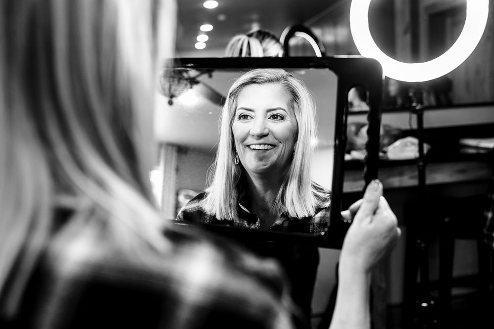 mother of the bride looks in mirror after having makeup finished