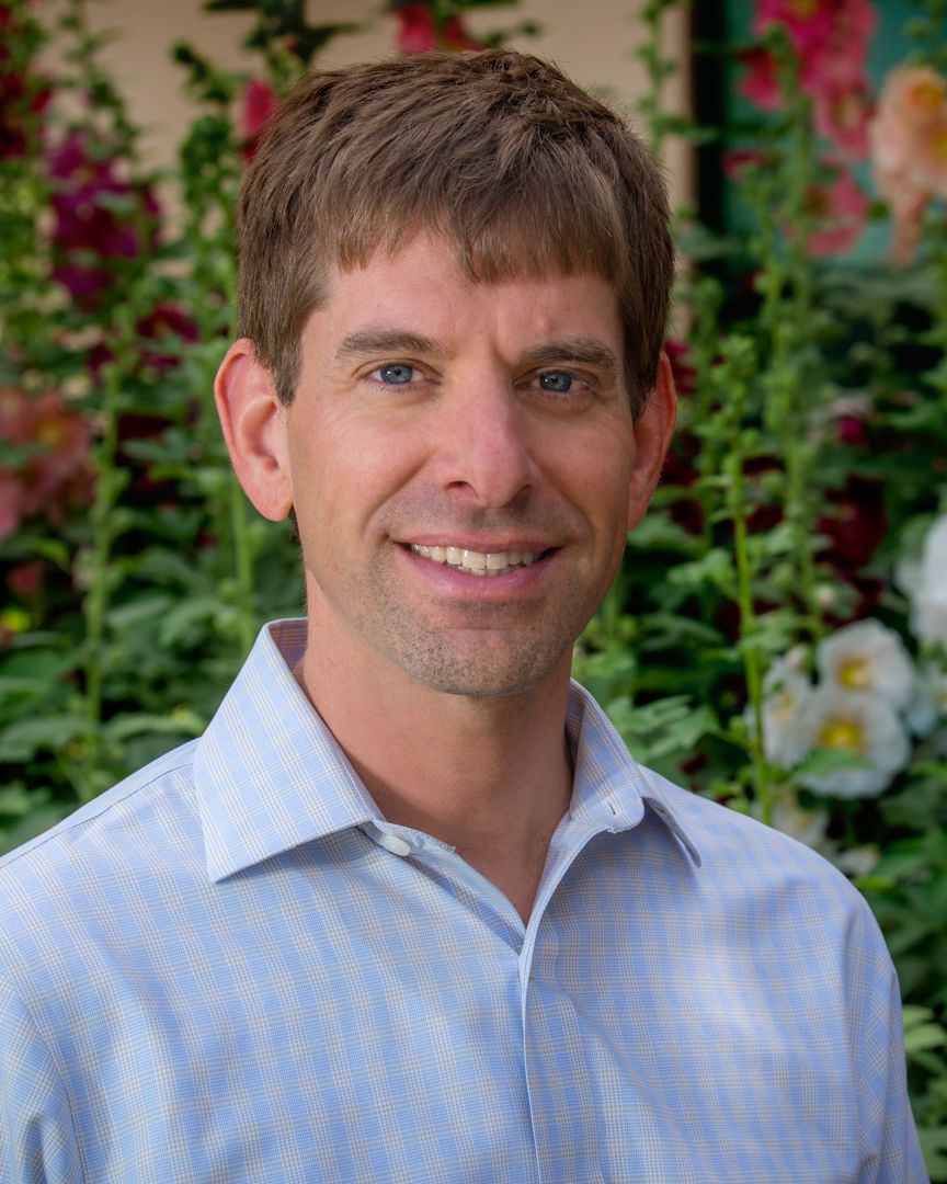 Headshot portrait of a man with flowers in background