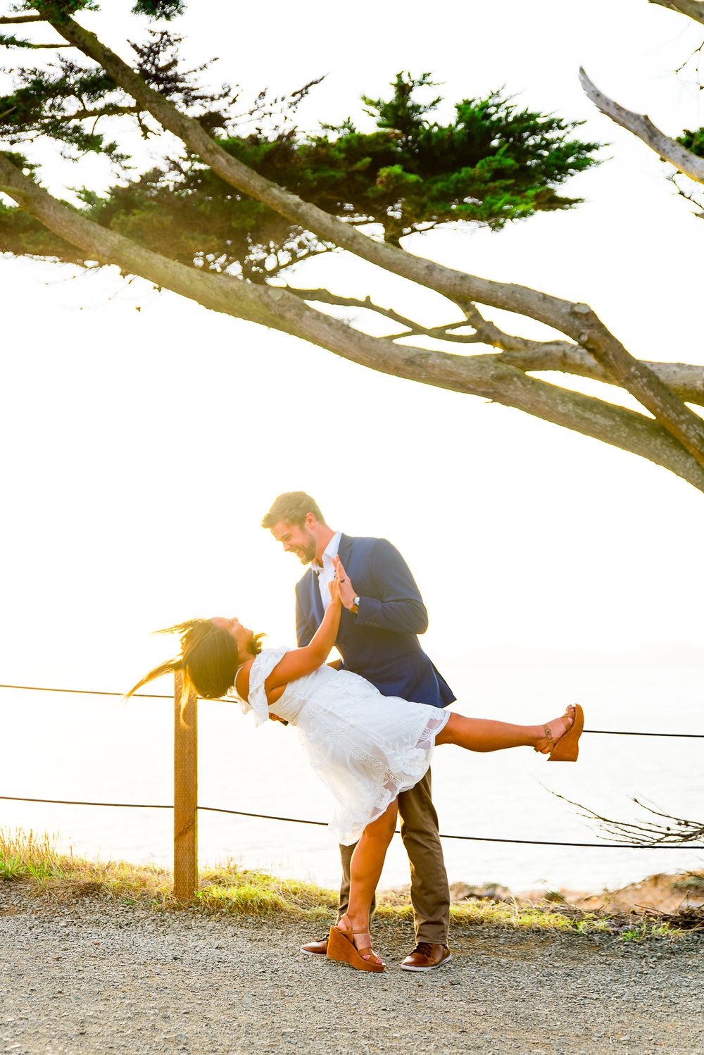 young man dipping his fiance in a white dress at sunset in San Francisco
