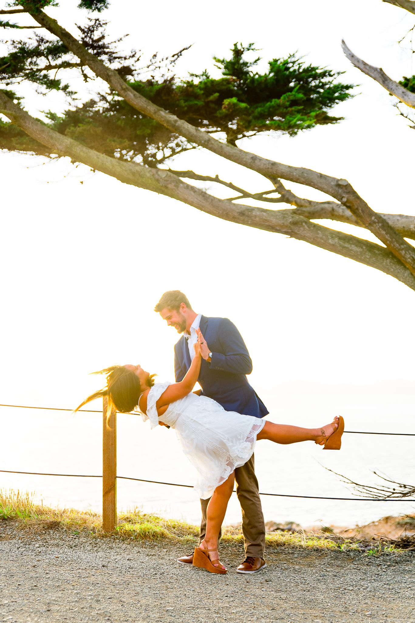 young man dipping his fiance in a white dress at sunset in San Francisco