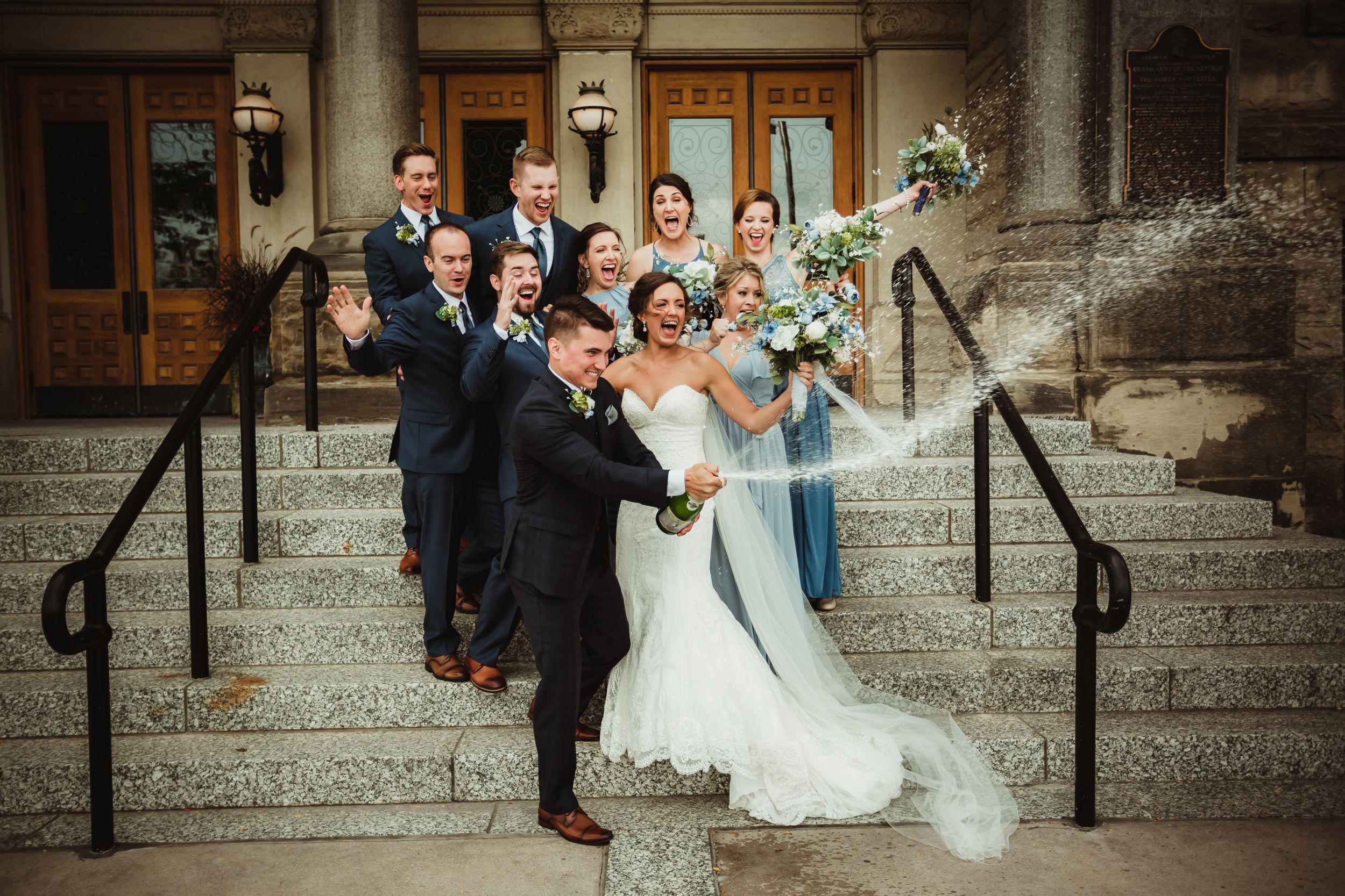 Wedding party standing on steps outside cheering and spraying champagne. and spraying champagne.