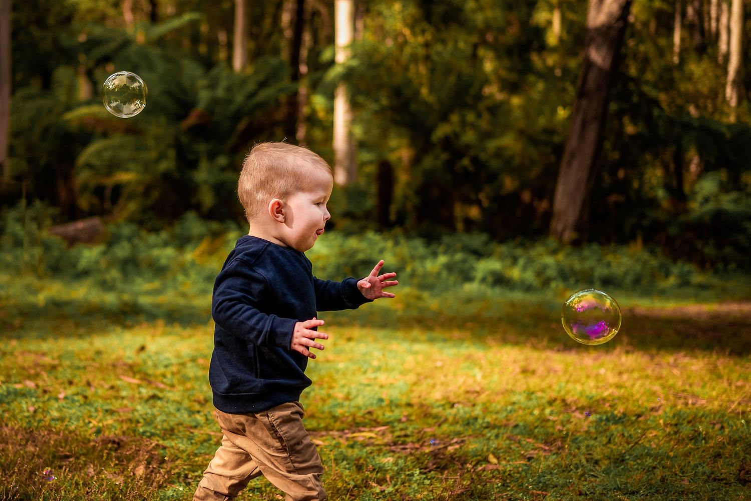 Blonde haired boy chasing bubbles in the forest