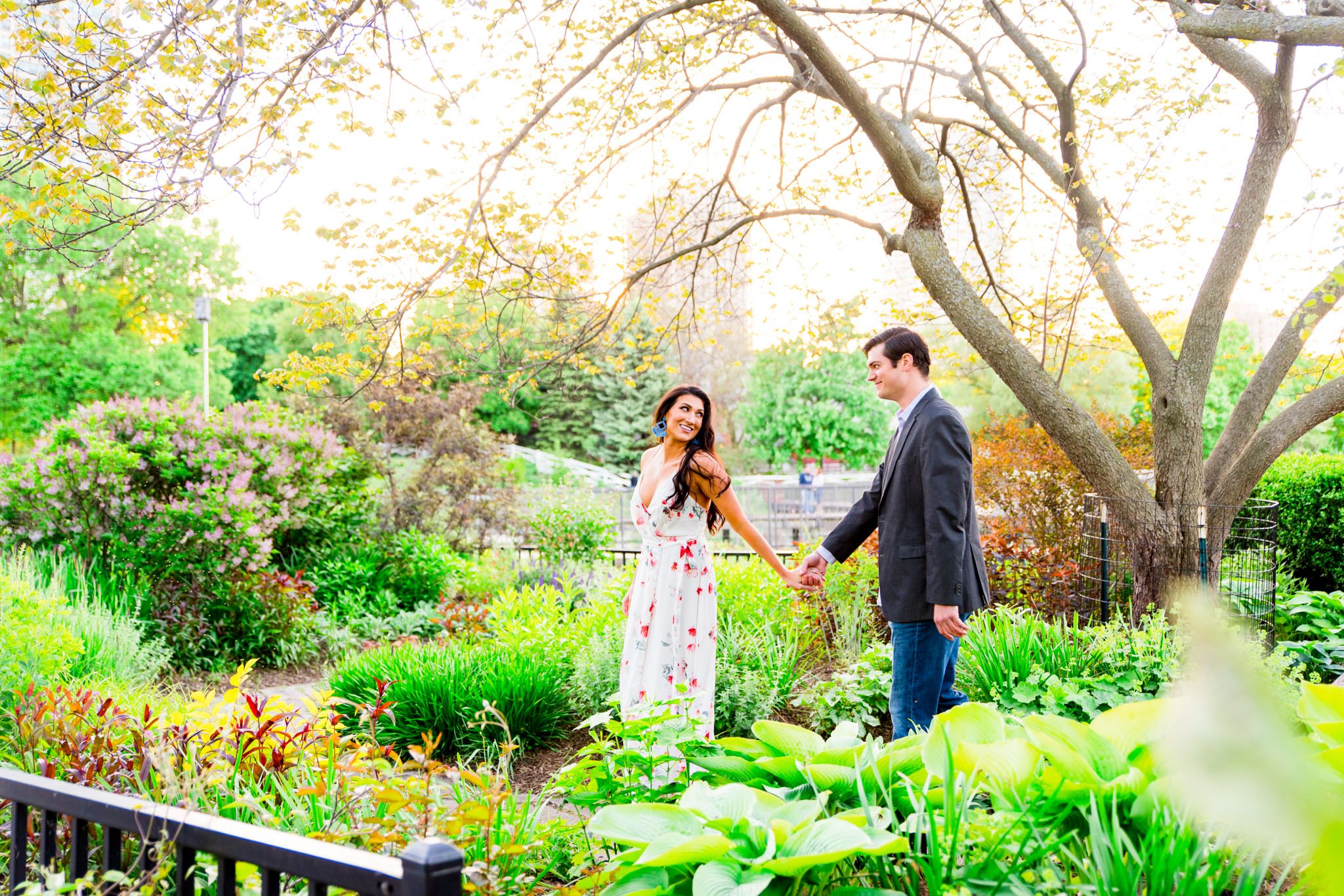 woman with long dark hair in a floral dress and blue macrame earrings leading fiance by the hand for engagement pictures