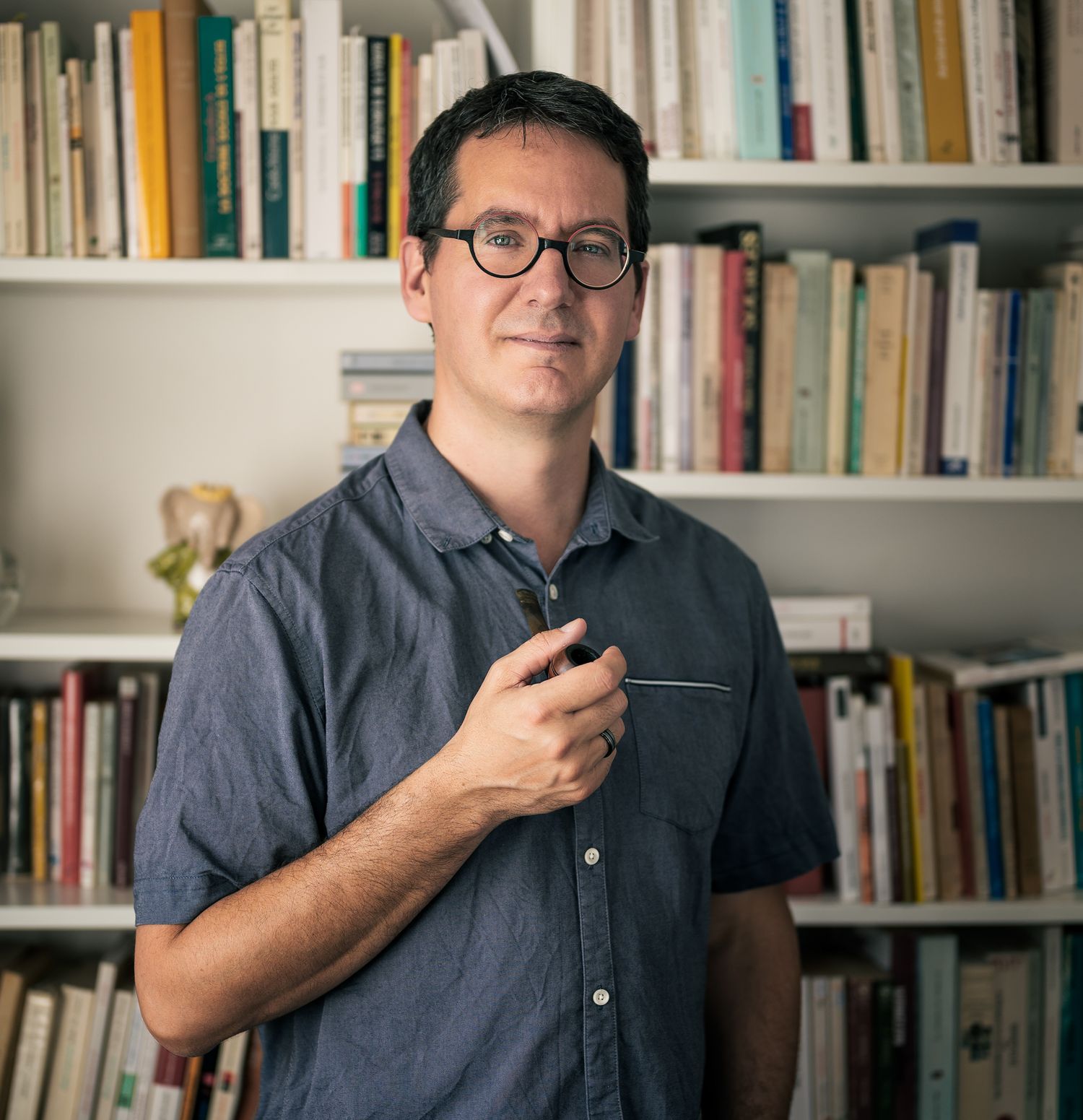Jeune théologien posant devant sa bibliothèque avec un éclairage naturel doux latéral