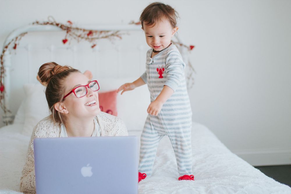 Lauren Cerna sitting on white bed with two year old son jumping
