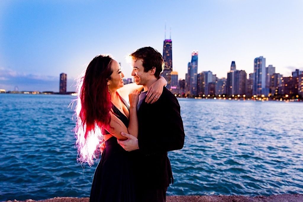 couple smiling at each other at night time with Chicago skyline behind them at North Avenue Beach