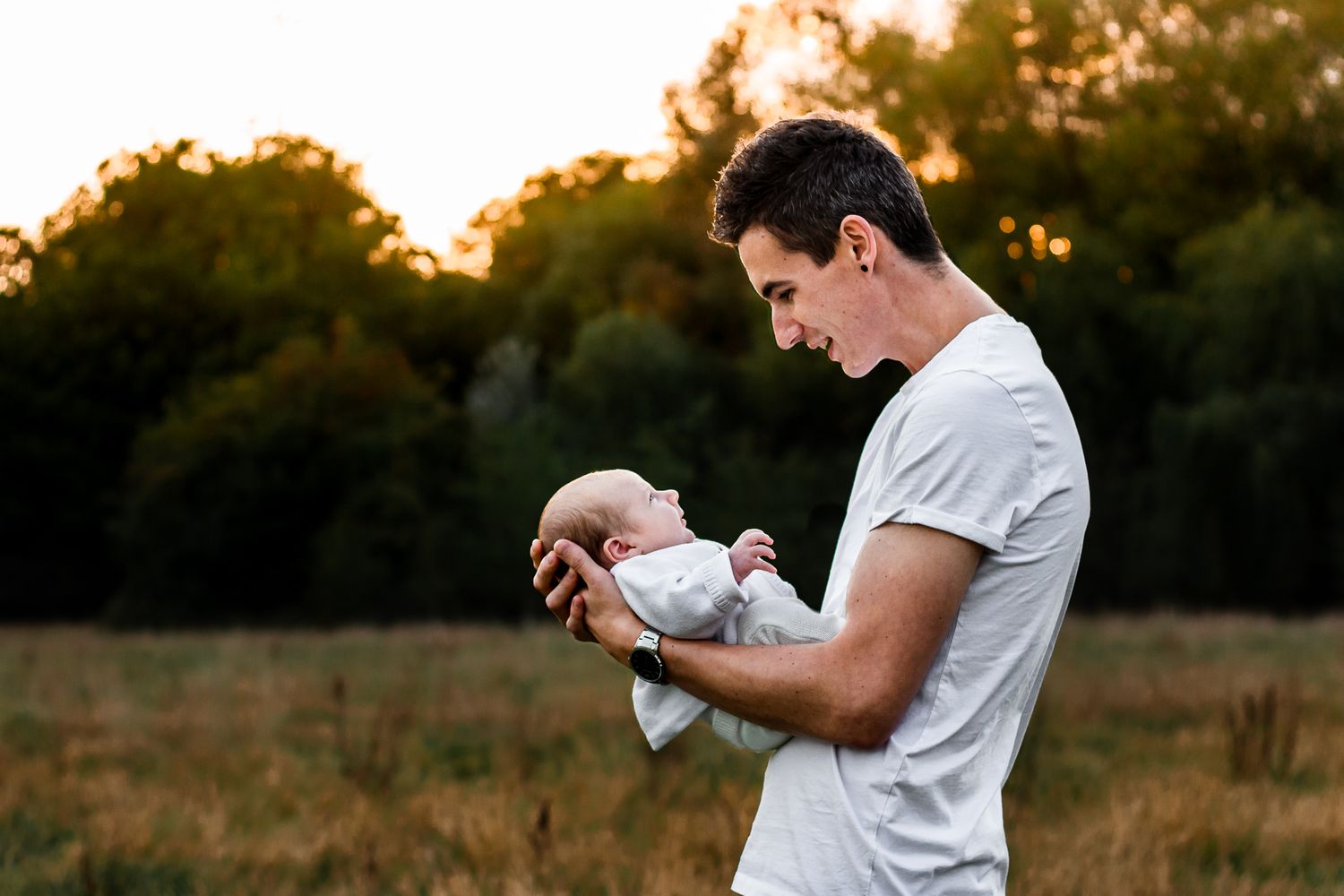 In a field in Havant, Hampshire, a new Dad holds his newborn baby boy while the sun sets behind them.