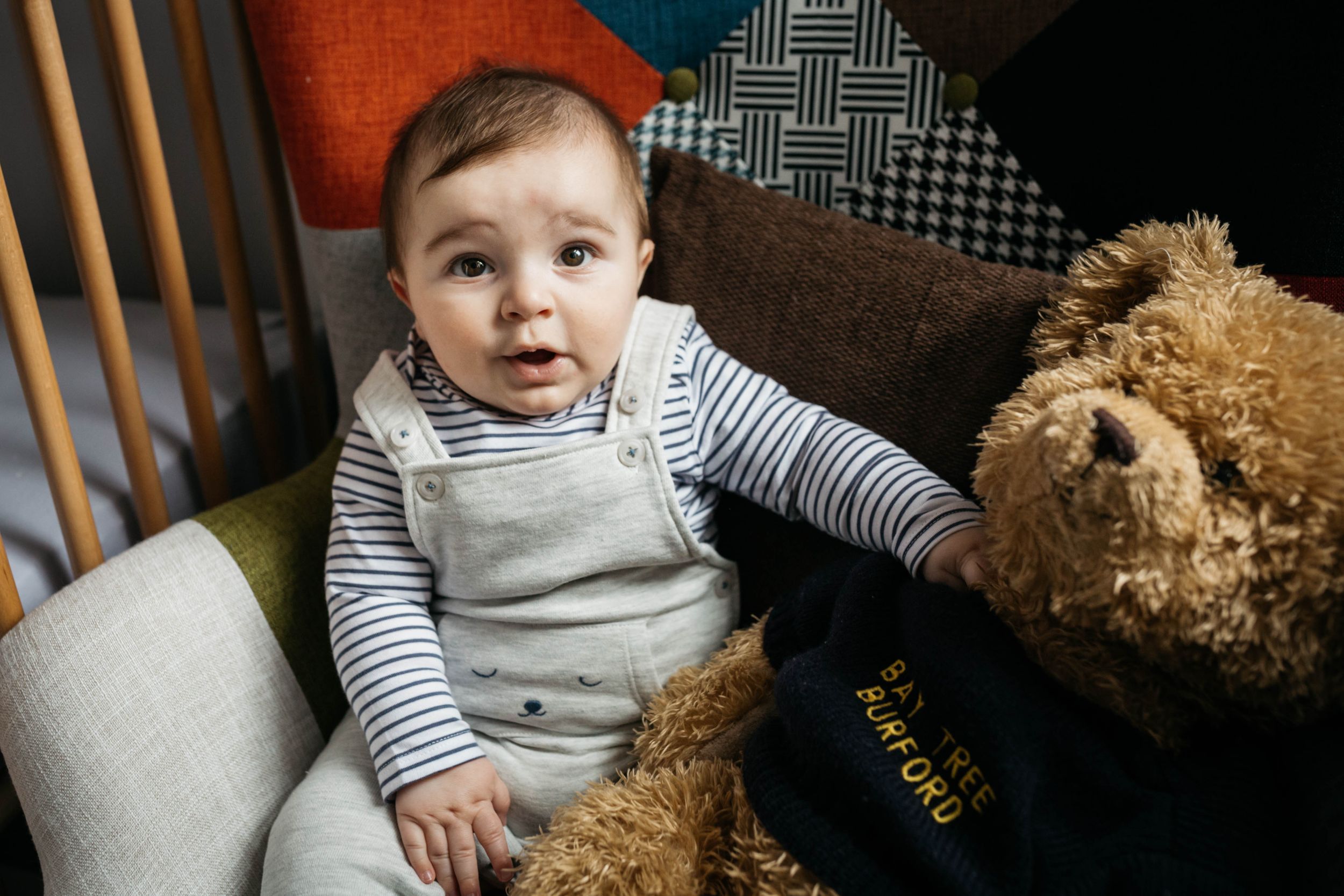 little baby boy sitting in patchwork armchair with cuddly teddy