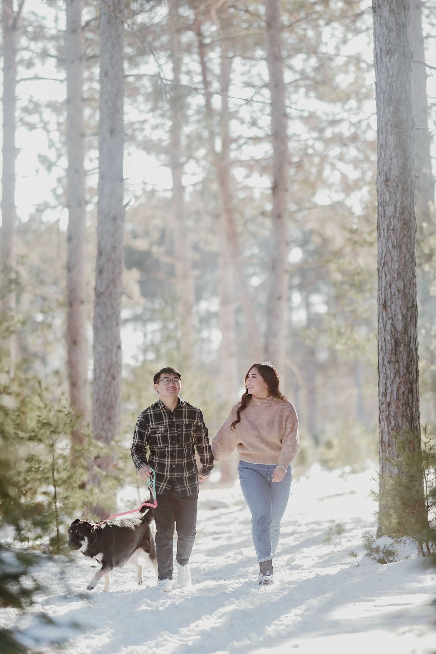 Couple strolls together on a snow-covered path through a serene winter forest.