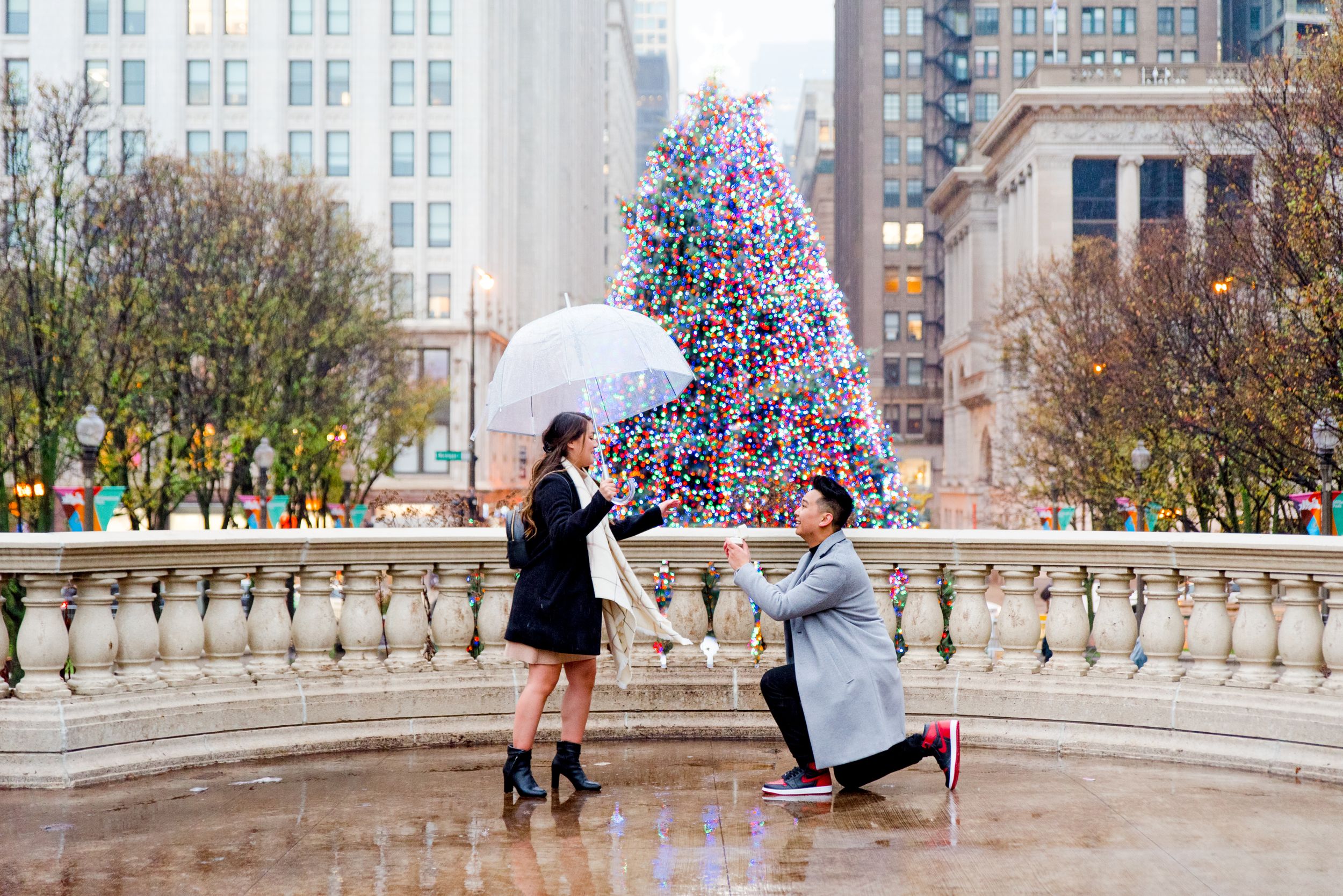 Man in gray coat kneeling down in front of Christmas Tree at Millennium Park in Chicago about to propose