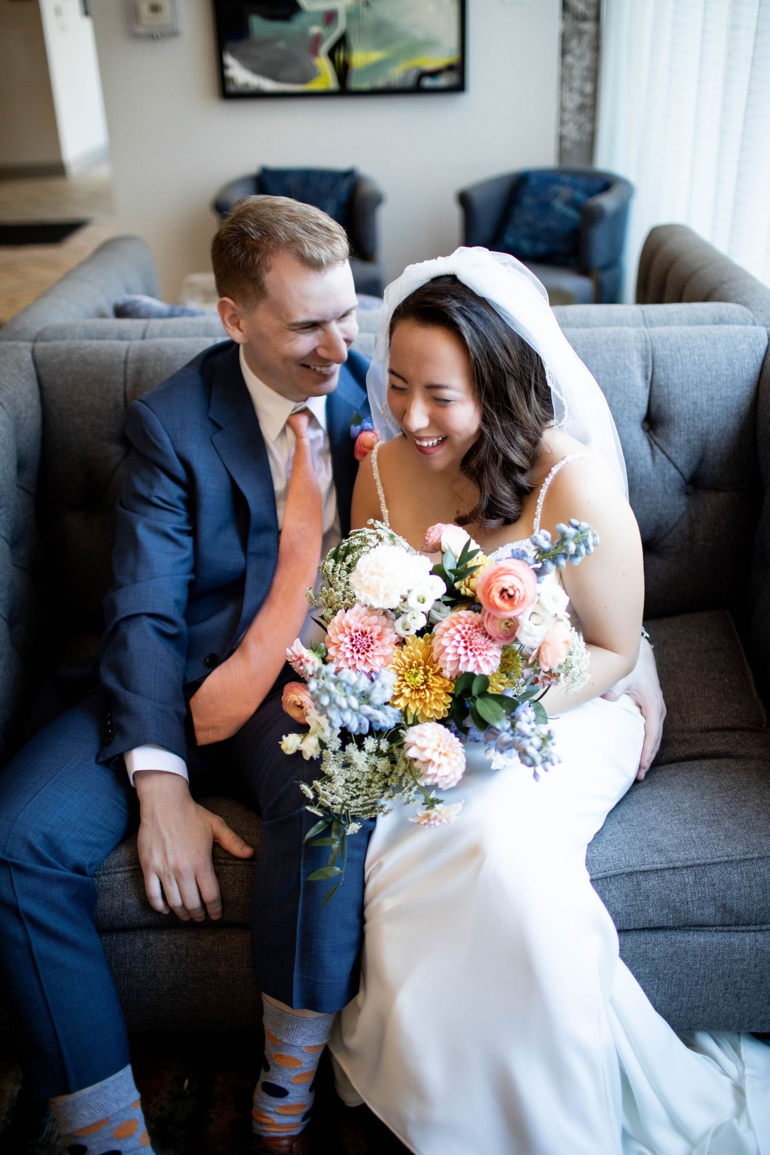 A joyful wedding moment captured on a grey couch with a colorful bouquet.