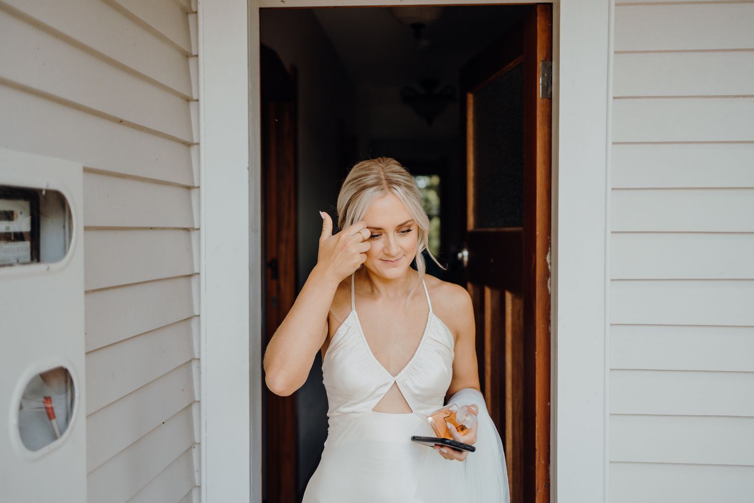 Someone in a white dress stands in a doorway holding a phone.
