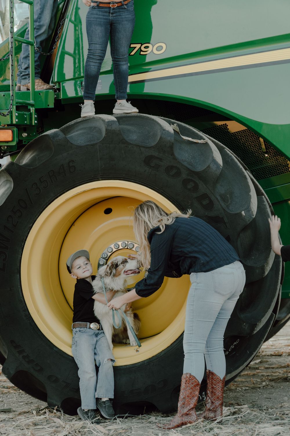 People interacting near the large wheel of a John Deere combine harvester.