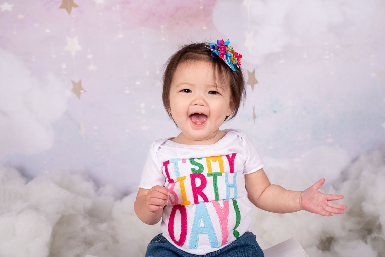 Little Girl laughing during her 1st birthday session with a sky,stars and clouds pastel backdrop