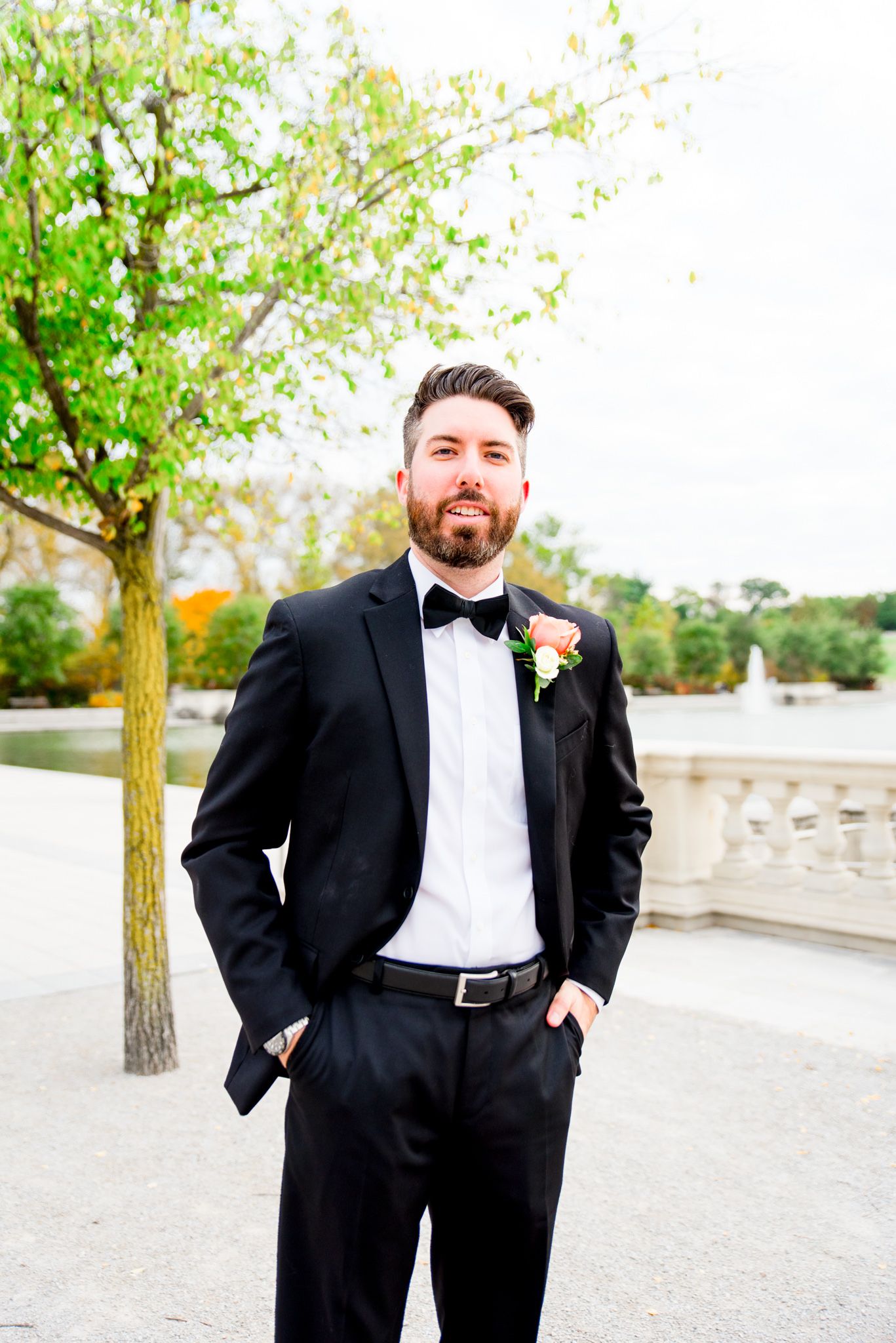 brunette groom with beard in black suit and bowtie smiles off to the side for St. Louis fall wedding at Forest Park