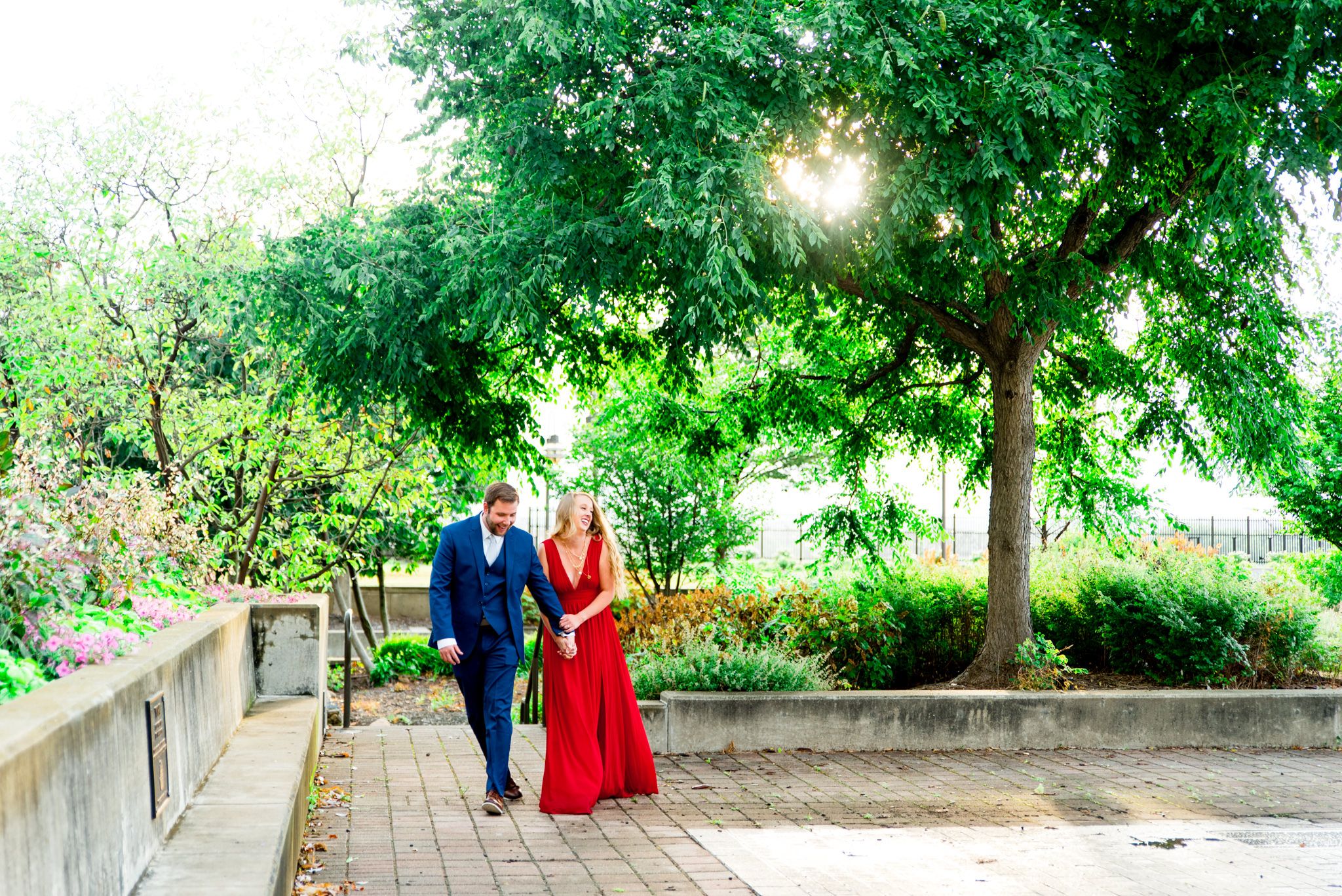 couple in red dress and navy suit walk through park at the Galt House Hotel