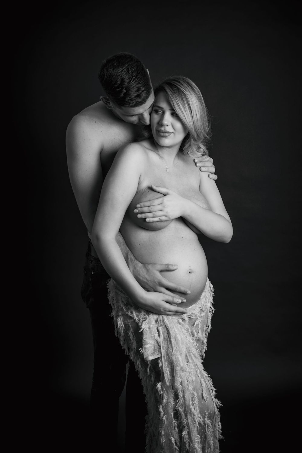 hugged couple standing together and holding belly bump