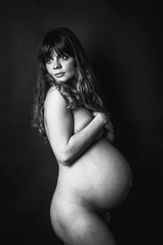 pregnant woman looking behind shoulder holding her breasts and posing