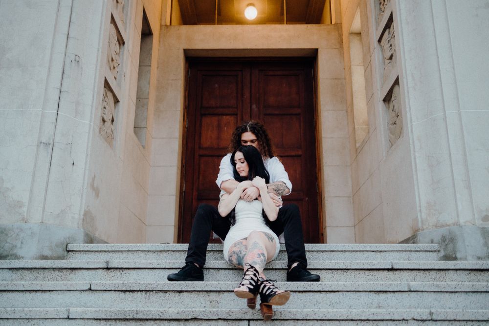 A couple sits on stone steps in front of a grand wooden door entrance.