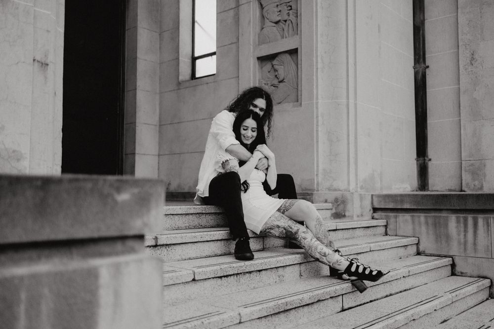 A black and white photo of a couple sitting on stone steps of a classical building.